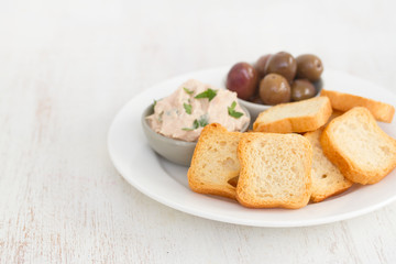 toasts with fish pate and olives on white plate