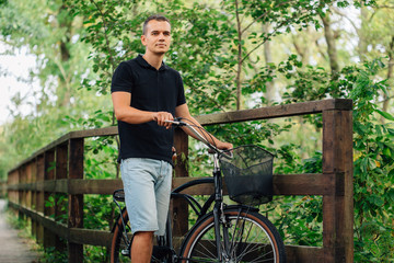 Naklejka na ściany i meble Pretty young man in casual standing with retro bicycle in park