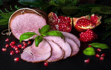 Smoked ham with herbs, fruits (pomegranate) on black background