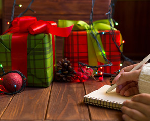 The girl holds a notebook for recording the plans for the next new year, in the background Christmas gifts