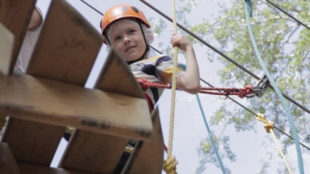 Little cute boy enjoying activity in a climbing adventure park on a summer sunny day. toddler climbing in a rope playground structure. Safe Climbing extreme sport with helmet and Carabiner. insurance