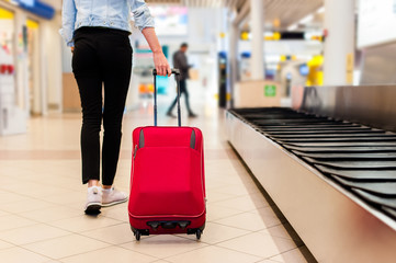 Close-up of young woman back side at the airport, carrying her trolly bag.