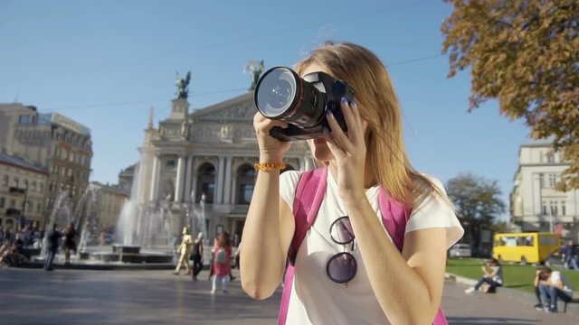 Pretty caucasian fair hair tourist girl, with a pink backpack, is taking a photo in front of the Opera House and fountain in the background, sunny day, slow motion