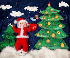 Infant baby boy wearing Santa costume holding bag with gifts.