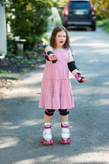 Fototapeta premium Young girl outside learning to riding on roller skates on driveway wearing protective elbow, wrist and knee pads
