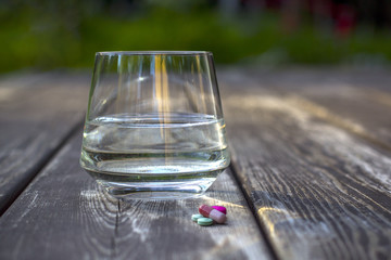 Pills and glass of water on wood background