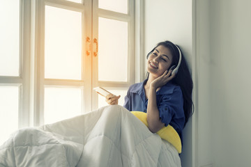 Asian women listen to music in their wireless headsets in the window and smile happily.