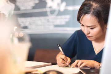 Obraz premium Close up of a Asian businesswoman writing about plan of business while meeting with colleague in meeting room at coffee shop on weekend in selective focus.