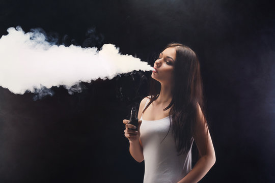 Young Woman Vaping E-cigarette With Smoke On Black