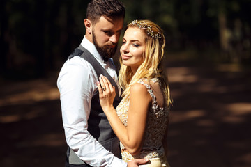 Stylish couple of happy newlyweds posing in the park on their wedding day. Perfect couple bride, groom posing and kissing 
