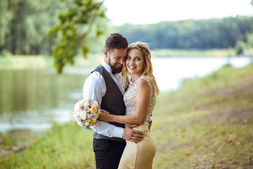Stylish couple of happy newlyweds posing in the park on their wedding day. Perfect couple bride, groom posing and kissing 
