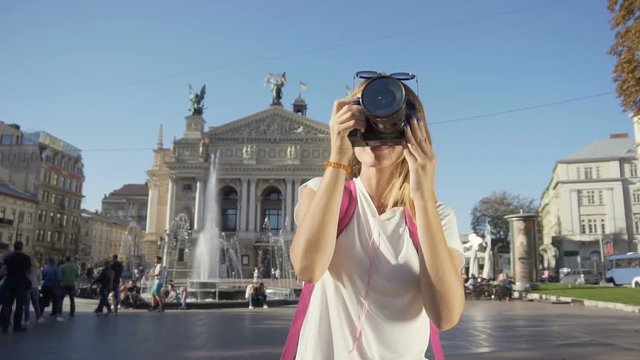 Attractive caucasian fair hair tourist girl, with a pink backpack, is taking a photo in front of the Opera House and fountain in the crowdy, busy street, sunny day, slow motion