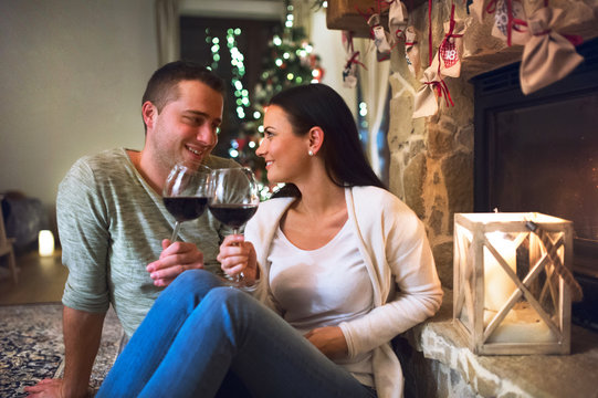 Couple sitting in front of fireplace, drinking wine.
