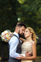 Stylish couple of happy newlyweds posing in the park on their wedding day. Perfect couple bride, groom posing and kissing 
