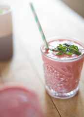 glass of strawberry smoothies on a wooden table over light from window