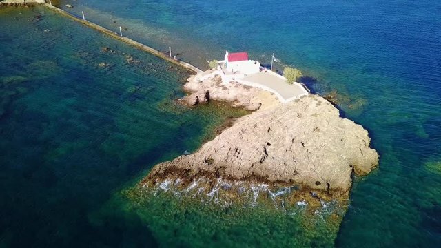 August 2017: Aerial drone video of iconic chapel of Agios Isidoros built in a rock next to the coast with clear turquoise waters, Leros island, Aegean, Dodecanese, Greece