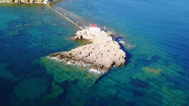 August 2017: Aerial drone video of iconic chapel of Agios Isidoros built in a rock next to the coast with clear turquoise waters, Leros island, Aegean, Dodecanese, Greece