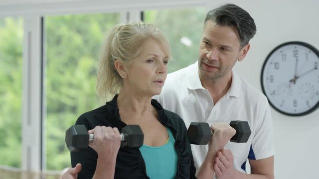  Healthy mature woman working out in the gym with personal trainer