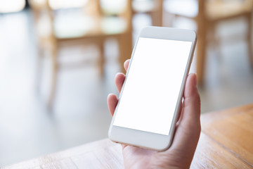 Mockup image of hand holding white mobile phone with blank screen on table in cafe
