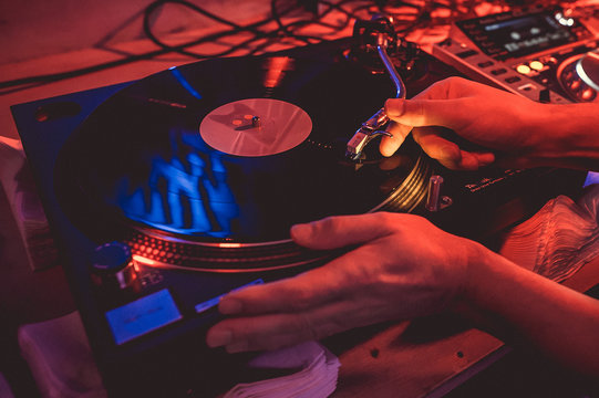 Hands of a DJ putting a vinyl record on a record player in a music club in the rays of blue and red light