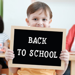 Cute boy holding blank blackboard in classroom, education concept background