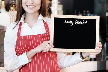 Smiling woman holding blank daily special board over blur cafe background, copy space for text,...