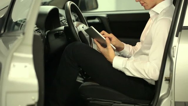 Elegant businessman browsing internet on tablet while sitting in the car
