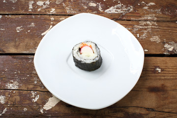 Sushi. One roll on a white plate. The wooden background is rough.