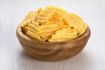 Bowl with potato chips on a wooden background.