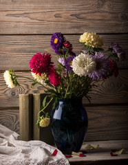 Asters in blue vase on table on wooden background wall.