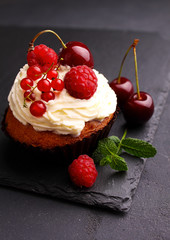 homemade cupcake with a cream, decorated with mint and berries on a black background.