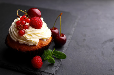 homemade cupcake with a cream, decorated with mint and berries on a black background.