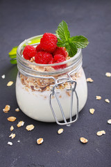 healthy breakfast: yogurt with muesli and raspberries on a black background