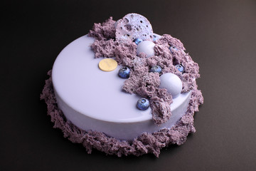 Cake with blackberry mousse in the mirror glaze decorated with a molecular biscuit. On the black background.