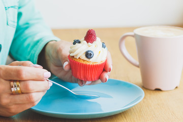 Fototapeta na wymiar Woman's hands with a cup of coffee and a cupcake on the plate