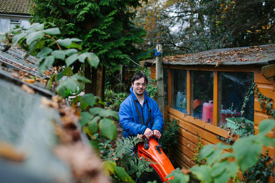 Smiling Down's syndrome man using a leaf blower in a garden.