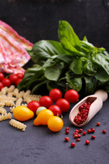 italian food: pasta, basil, tomato, olive oil on a black background, copy space.