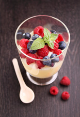 Milk pudding with berries in a glass on a black background