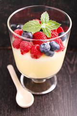 Milk pudding with berries in a glass on a black background