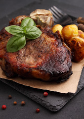 Steak on a bone baked with vegetables: potatoes, garlic, onions. Black background