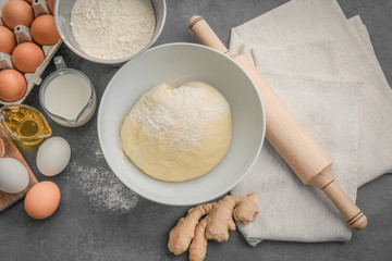 Raw dough in bowl and ingredients on kitchen table