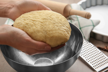 Female chef holding dough over bowl on kitchen table