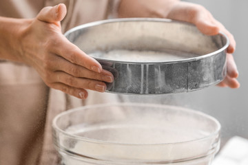 Female chef sifting flour into glass bowl, closeup