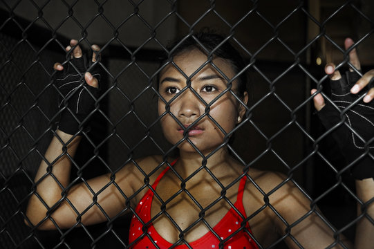 beautiful and sexy Asian fighter woman in fighting gloves and sport clothes inside MMA cage posing cool