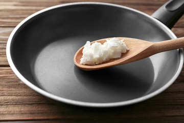 Wooden spoon with coconut oil in frying pan on table