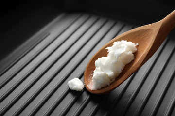 Wooden spoon with coconut oil in frying pan, closeup