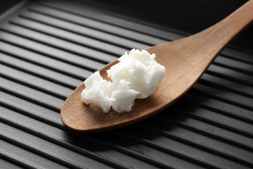 Wooden spoon with coconut oil in frying pan, closeup