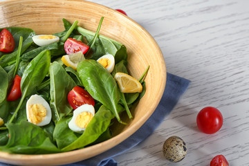 Salad with spinach leaves and eggs in bowl on wooden table