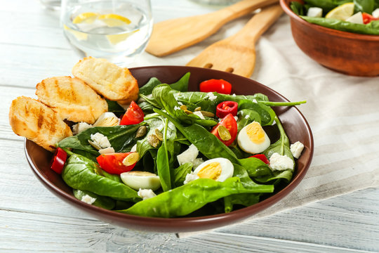 Plate of tasty salad with spinach leaves  on wooden table
