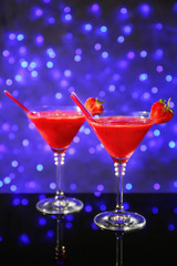 Glass of delicious strawberry daiquiri on table against defocused lights